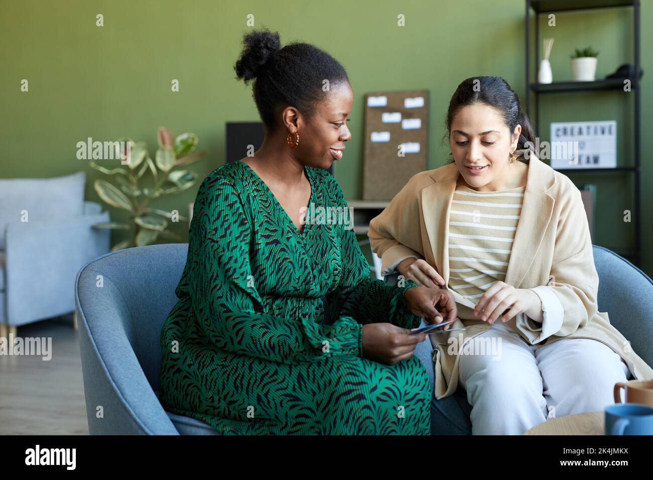 Felice giovane designer afro-americano che mostra le foto al collega durante la discussione di nuove idee per il progetto creativo in ufficio Foto Stock