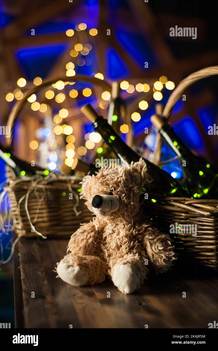 Orsacchiotto, bottiglia di champagne con cestino di Natale, ghirlande dorate su sfondo di legno marrone scuro, concetto di festa di Capodanno Foto Stock