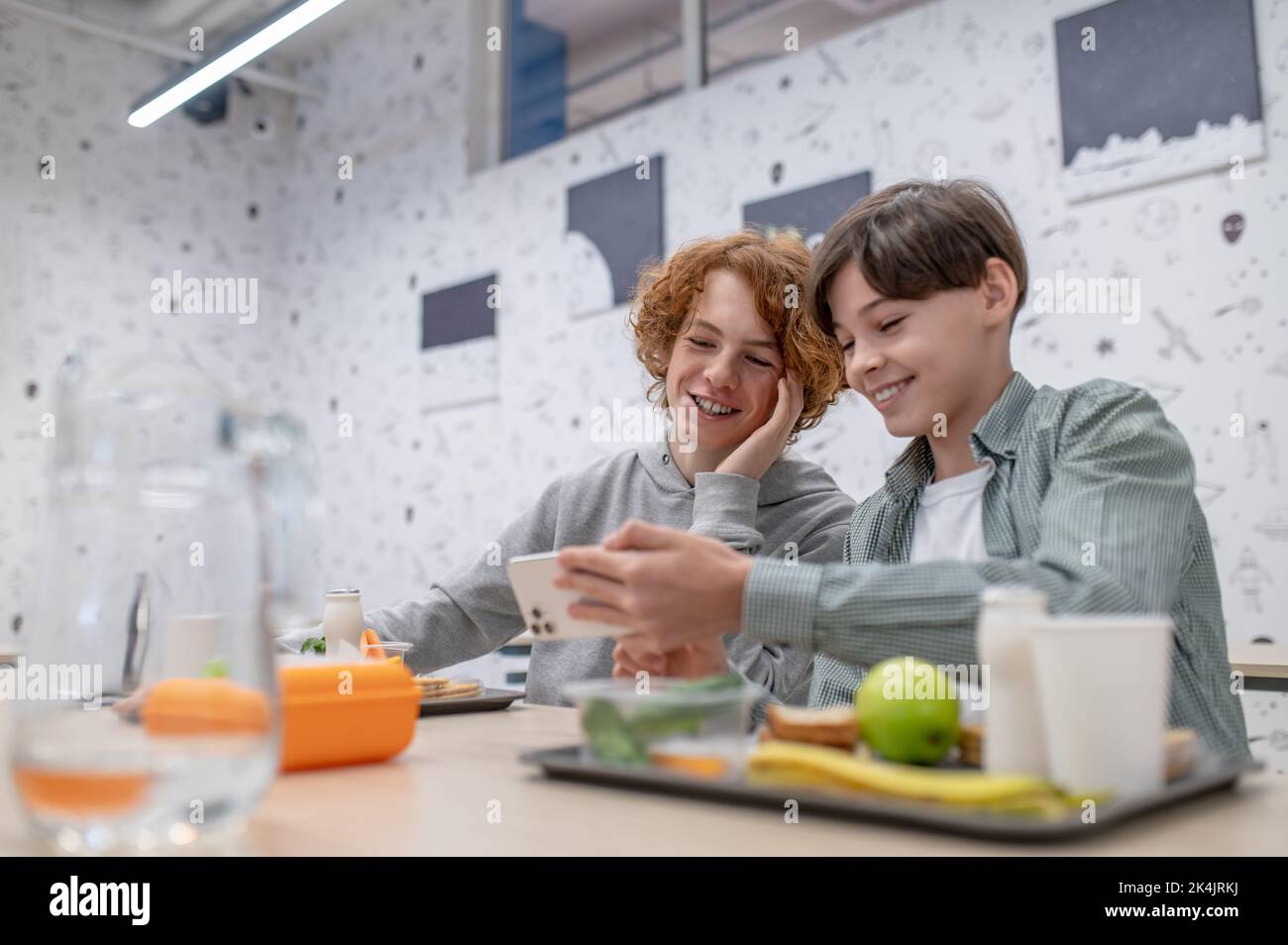 Due compagni di scuola allegri seduti nella mensa della scuola Foto Stock
