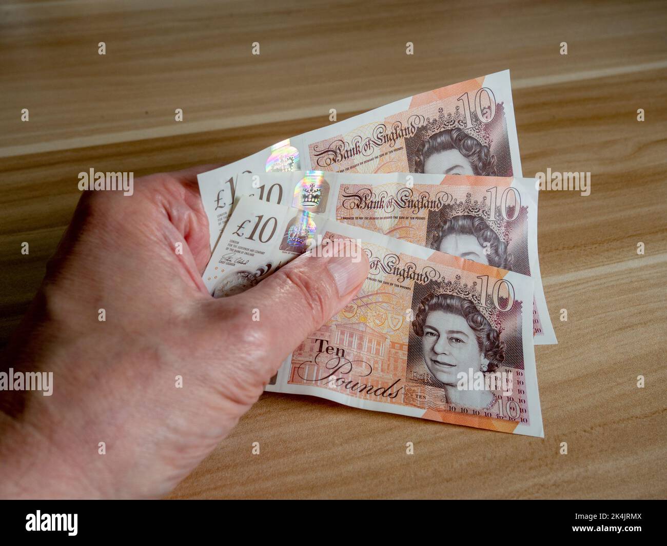 Mano dell'uomo che tiene tre note £10 che caratterizzano la testa della regina Elisabetta II - una delle molte cose che richiedono la modifica dopo la sua morte. Foto Stock