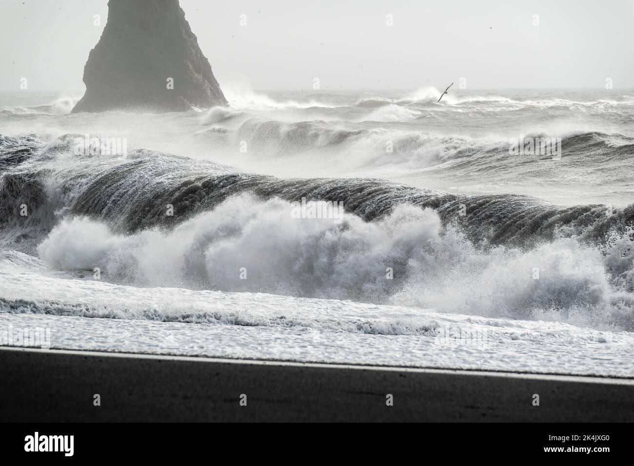 Onde oceaniche che si infrangono contro le pile di Reynisdrangar e la spiaggia di lava nera della spiaggia di Reynisfjara in un giorno tempestoso, vicino a Vík í Mýrdal, Islanda Foto Stock