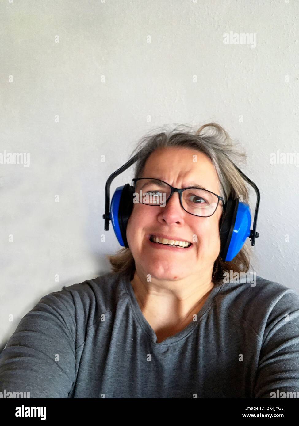 Frau mit Kopfhörer mit zerzausten Haaren, genervt vom Lärm Foto Stock
