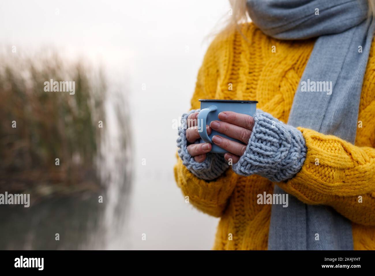 Donna che beve una bevanda calda dalla tazza in autunno freddo all'aperto. Mani femminili con guanto in maglia senza dita Foto Stock