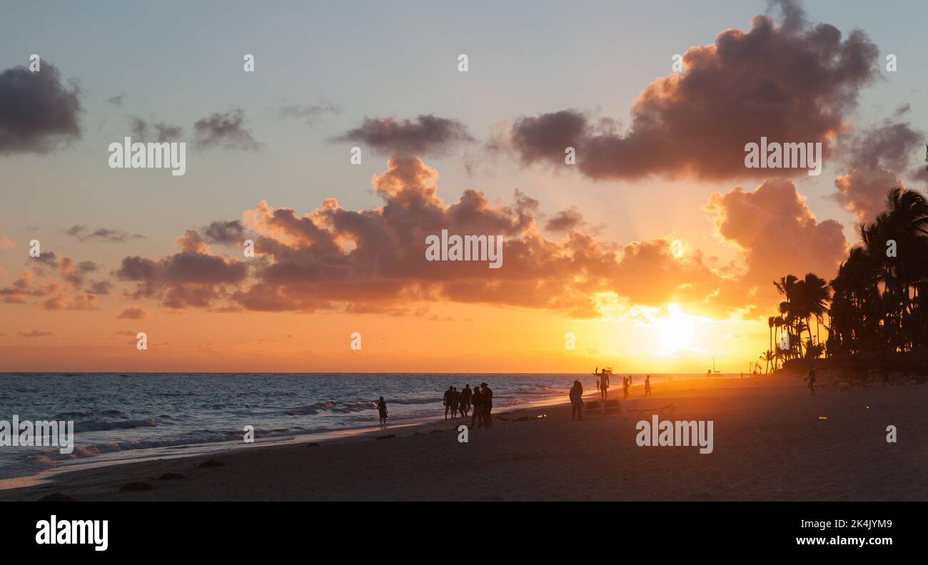 La gente cammina sulla spiaggia alla luce rossa del sole del mattino. Alba sulla spiaggia di Bavaro, repubblica Dominicana Foto Stock