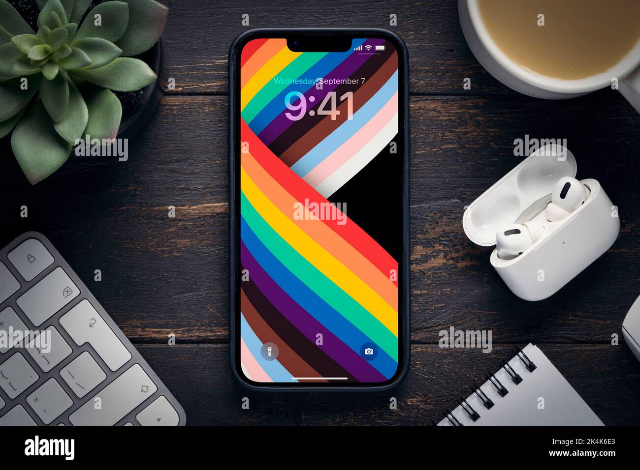 Il nuovo 14 iPhone pro max con lo screensaver originale sfondo arcobaleno sul tavolo circondato da oggetti d'ufficio - tastiere, cuffie Airpod, un Foto Stock