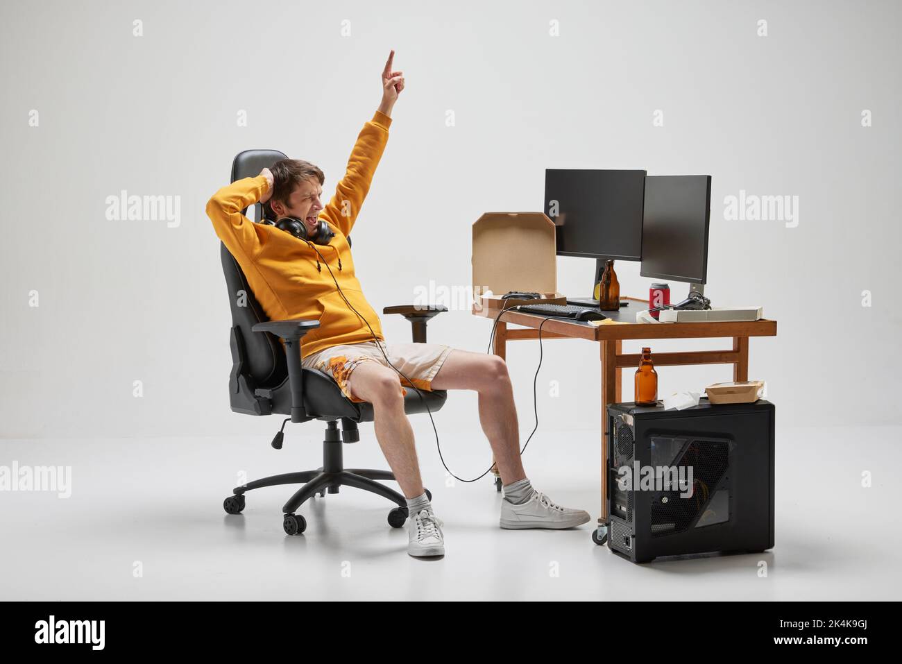 Giocatore. Giovane uomo in casa seduto a casa, giocando a giochi per computer isolato su sfondo grigio. Hobby, studio, educazione, gioventù, remoto Foto Stock