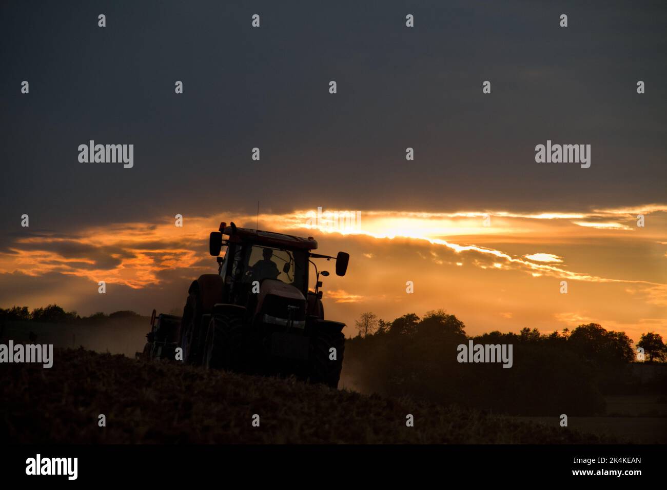 Trattore che erosa un terreno marrone rossastro, polveroso e argilloso in un paesaggio collinare al tramonto Foto Stock