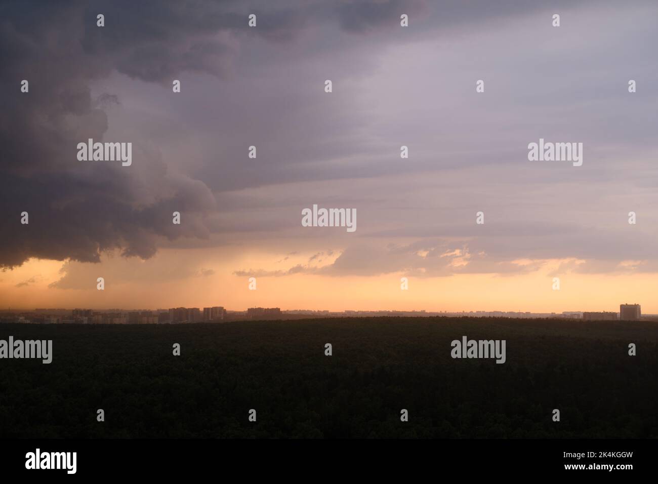Cielo tempestoso al tramonto con nuvole di pioggia scure. Pioggia su una foresta estiva con alberi verdi Foto Stock