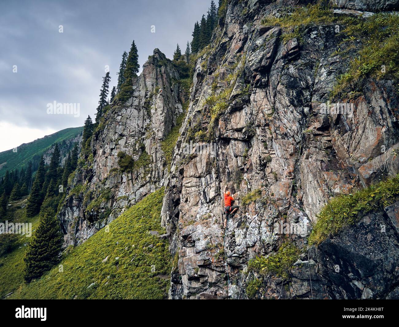 Fit forte atleta uomo in camicia rossa roccia arrampicata sulla parete verticale alta sulle montagne Tyan Shan in Kazakhstan Foto Stock