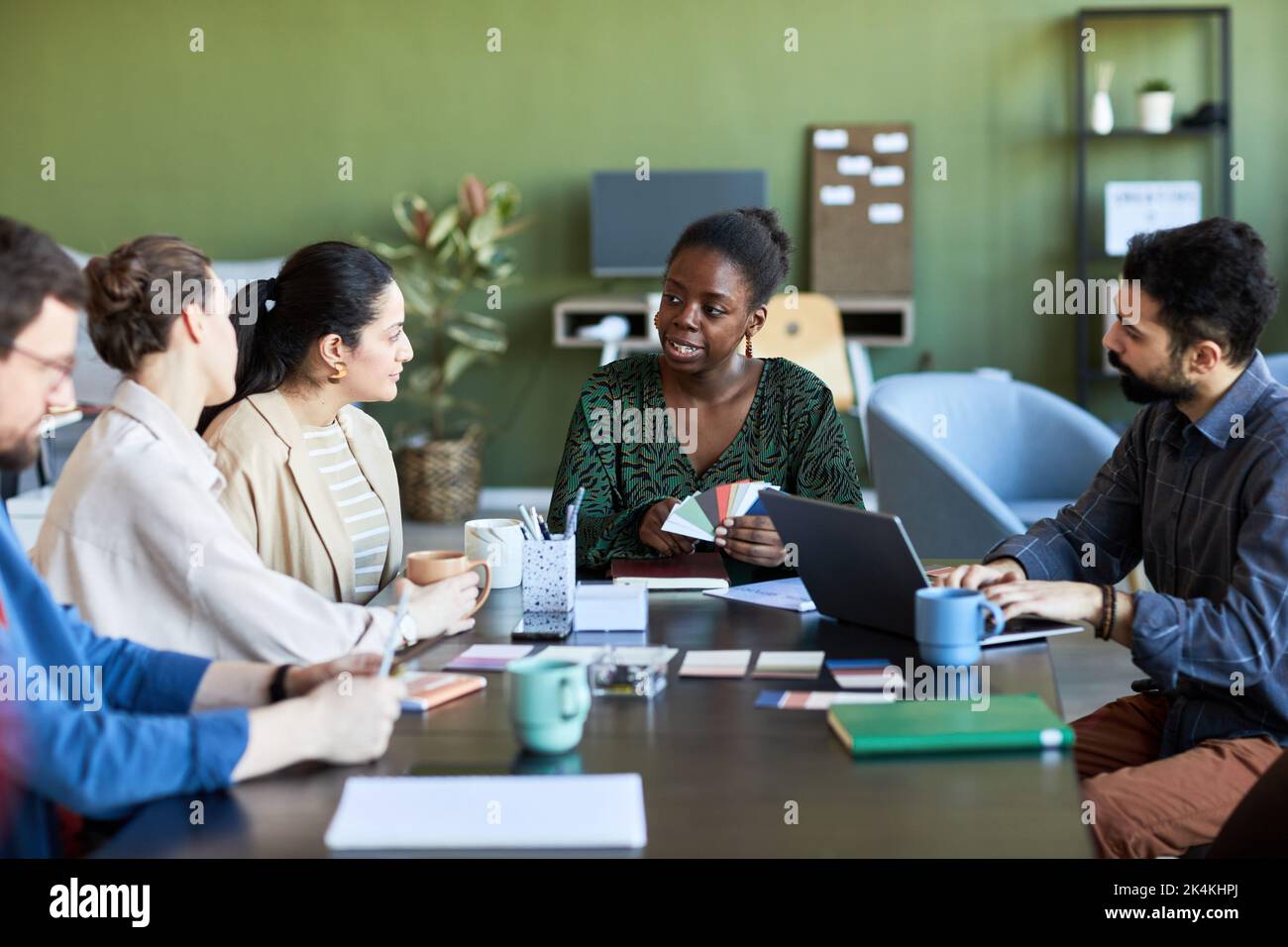 Donna d'affari afro-americana fiduciosa con tavolozza che spiega la sua opinione ai colleghi mentre guarda uno di loro alla riunione Foto Stock