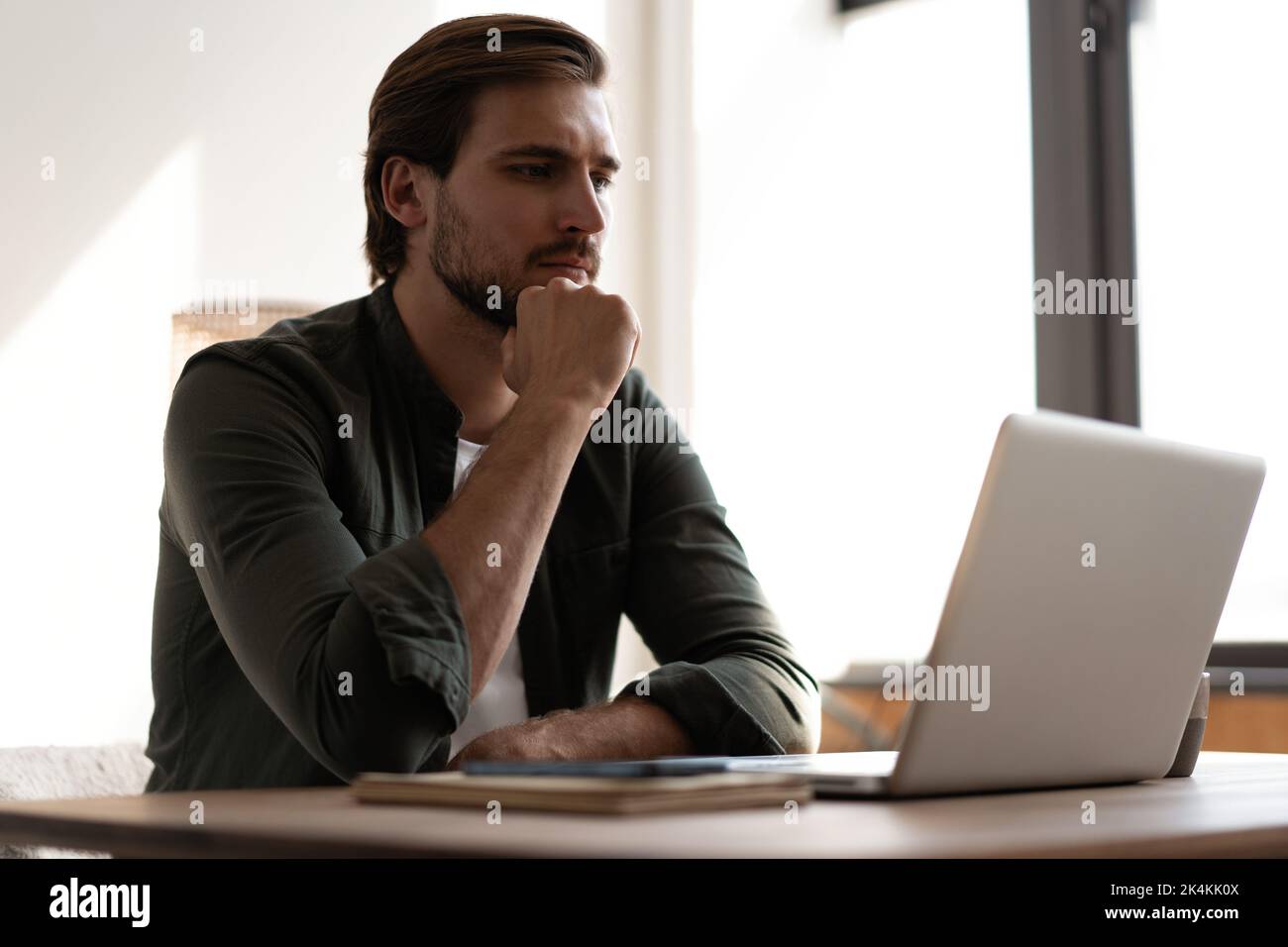 Uomo bearded pensivo seduto al tavolo di lavoro al laptop pensando alla soluzione del problema, impiegato premuroso ponderare considerando l'idea che guarda a compu Foto Stock