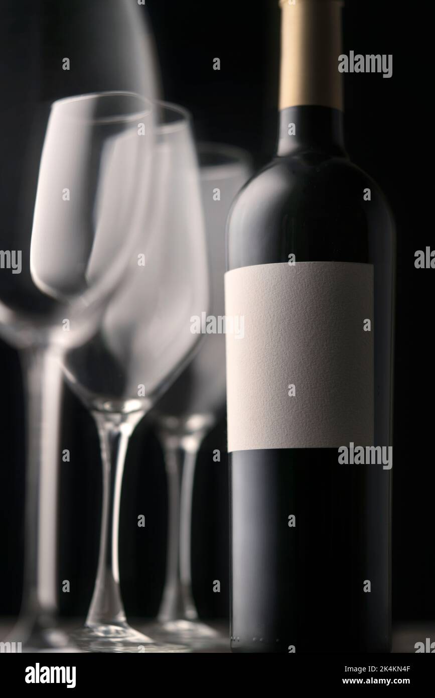 Un'elegante bottiglia di vino rosso con etichetta vuota e tre splendidi bicchieri da primo piano. Grafica minimalistica su sfondo nero Foto Stock