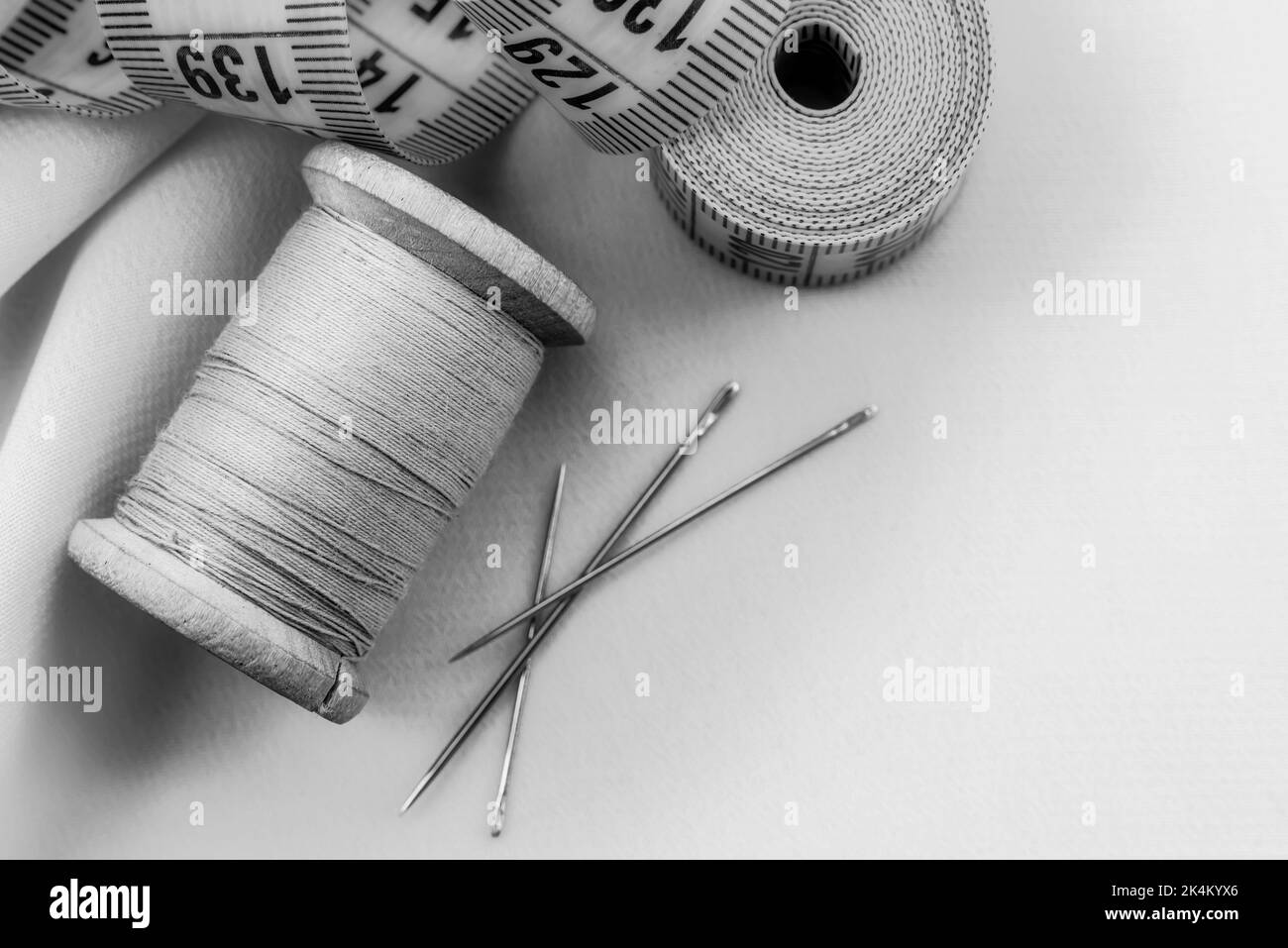 Ago retrò e filo giacciono sul tessuto. Attrezzi per un sarto o seamstress. Fotografia in bianco e nero Foto Stock