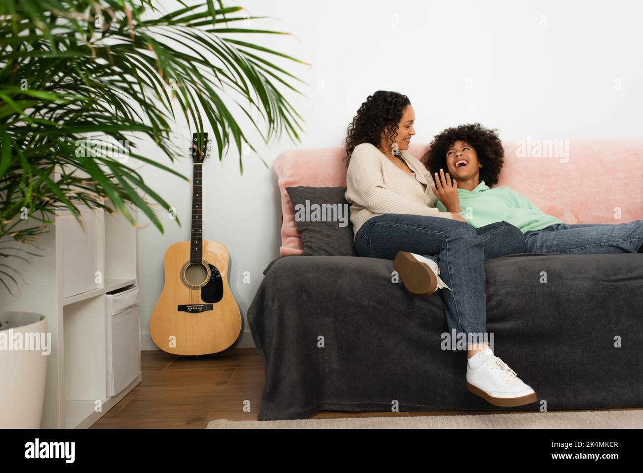 ragazza afroamericana eccitata che guarda la madre mentre riposa sul divano, immagine di riserva Foto Stock