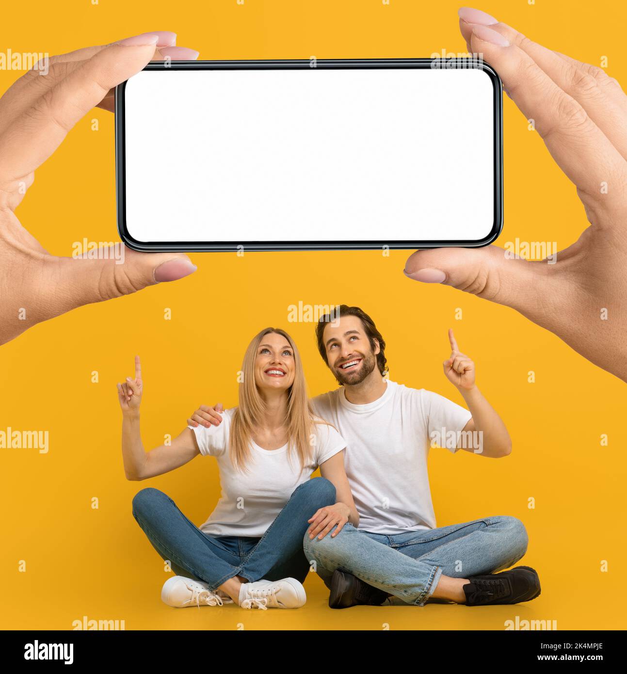 Felice uomo e donna europea millenario puntano le dita su un enorme smartphone con uno schermo vuoto nelle mani Foto Stock