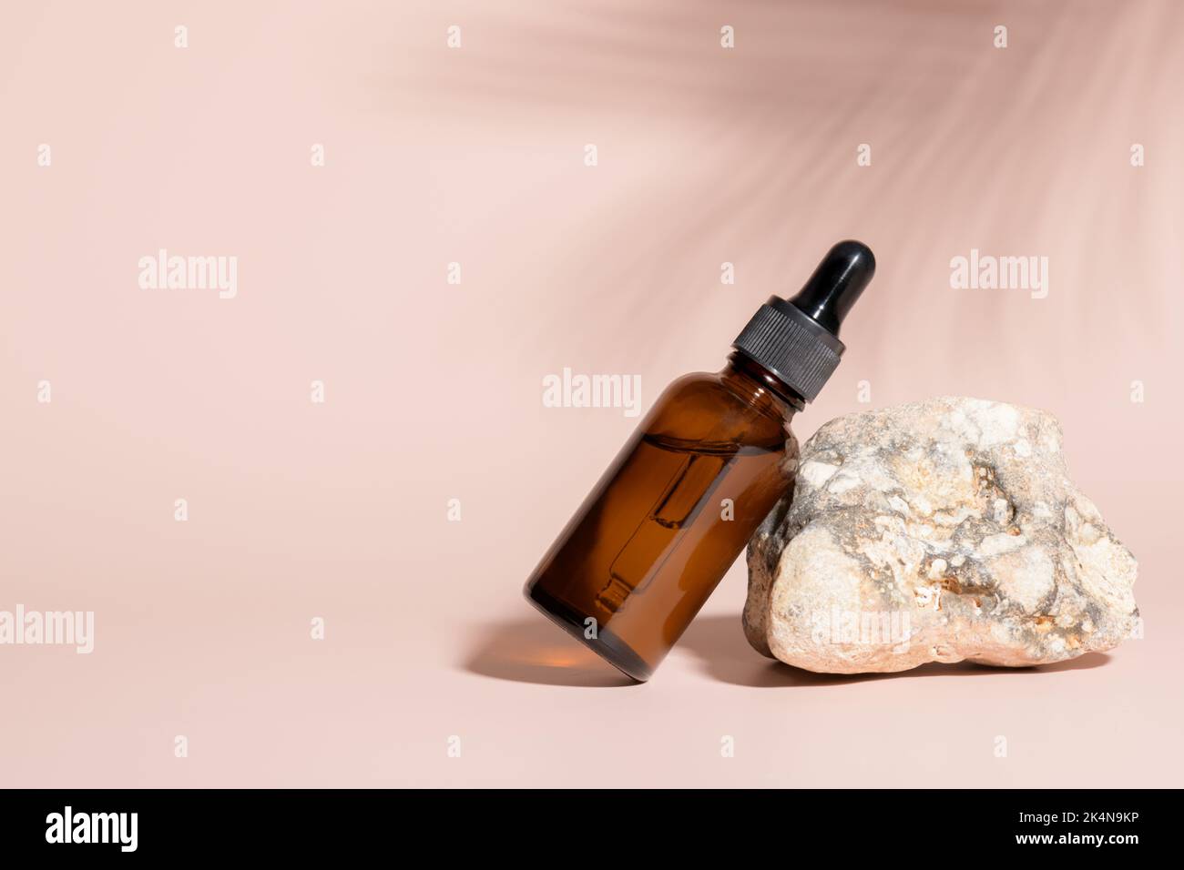 Bottiglia di vetro ambrato per siero su pietra con ombra di foglie di palmo su beige Foto Stock