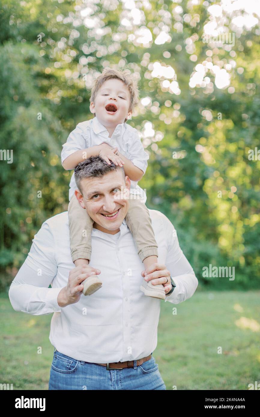 un ragazzo di 2-4 anni si siede sulle spalle del padre e sorride. Foto Stock