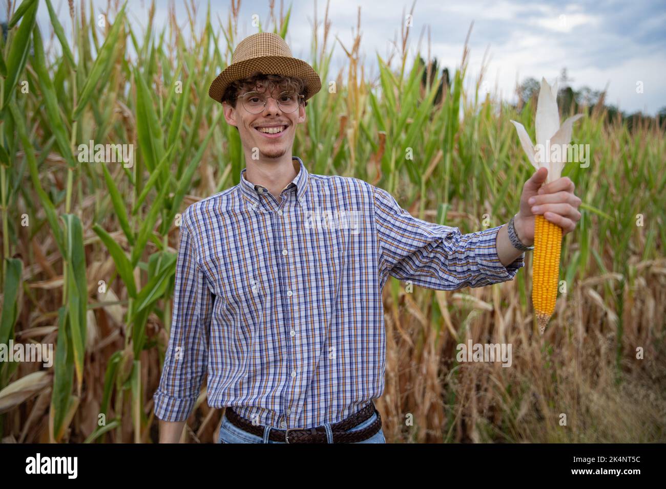 l'agricoltore che è molto orgoglioso della sua produzione di mais, sorride mostrando una grossa pannocchia. Foto Stock