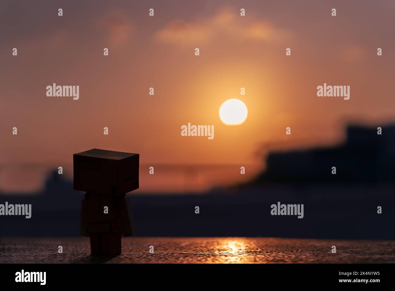 Una piccola figura carina di cartone che guarda fuori al tramonto dorato Foto Stock