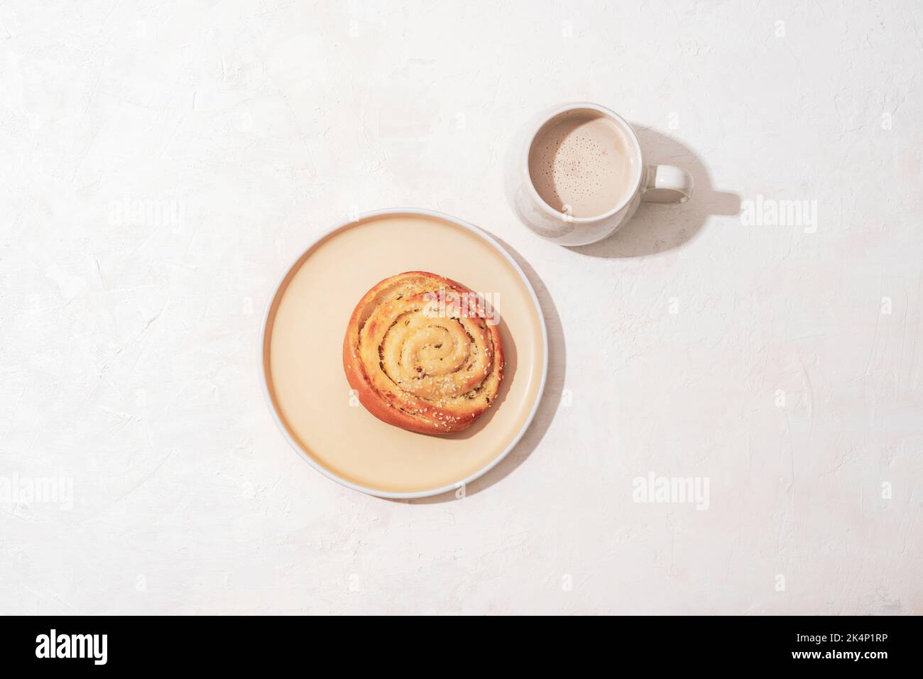 Panate su un piatto e il caffè con latte su un tavolo bianco. Concetto di colazione, ombre dure. Vista dall'alto, disposizione piatta. Foto Stock