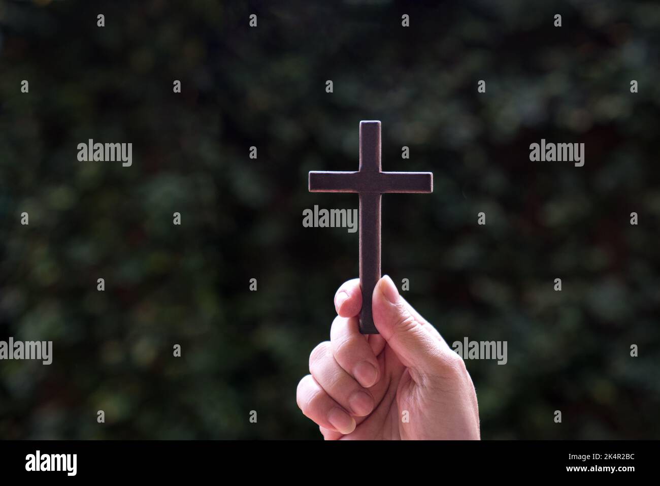 Mano che tiene una croce di legno con sfondo naturale. Concetto per la fede cristiana e il Venerdì Santo. Foto Stock