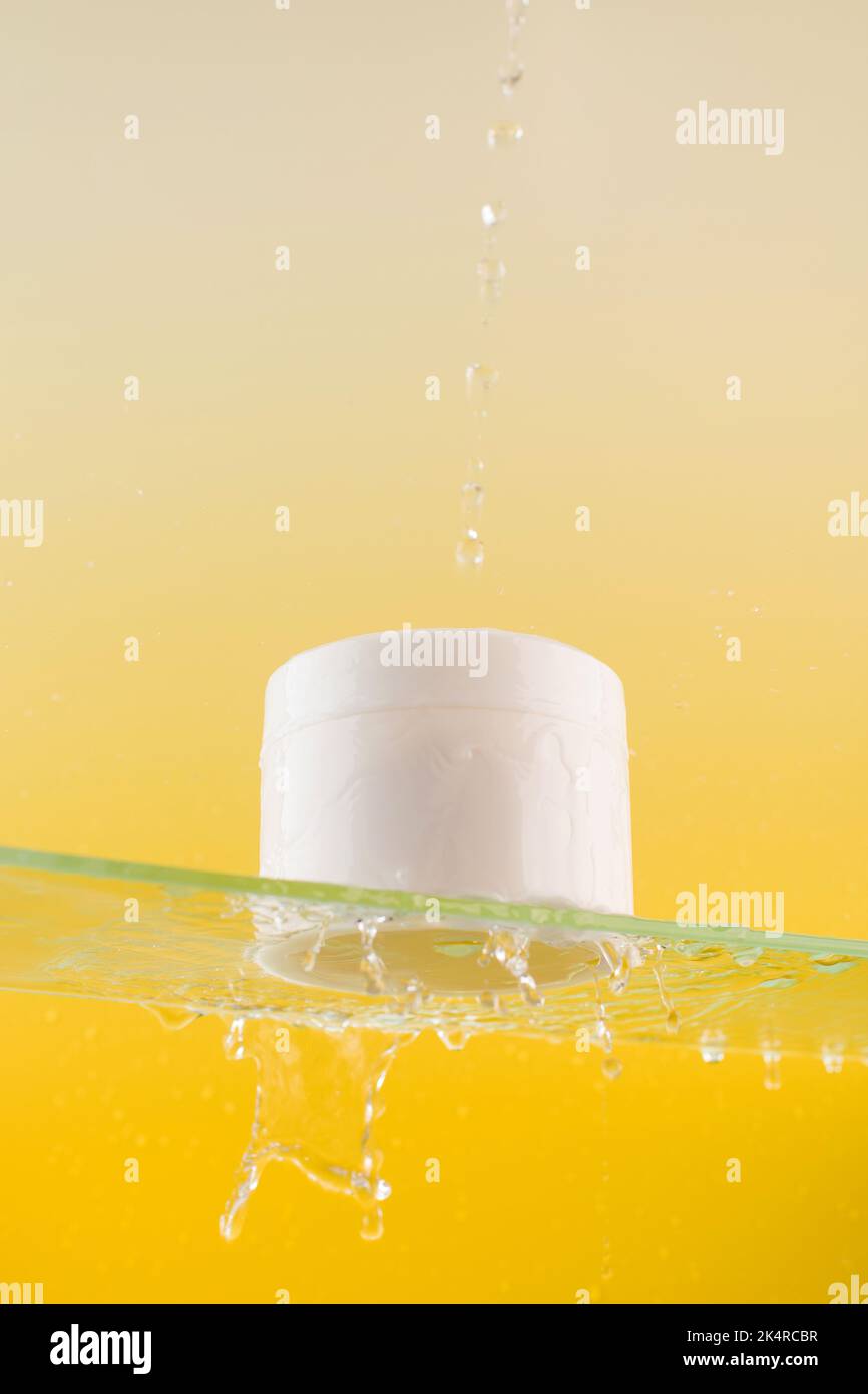 Vaso bianco con crema o maschera per viso e corpo con posto per il vostro logo su una mensola di vetro con spruzzi d'acqua Foto Stock