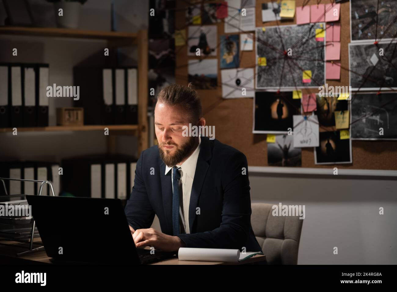 Il detective lavora in ufficio elaborando le prove utilizzando un computer portatile. Foto Stock