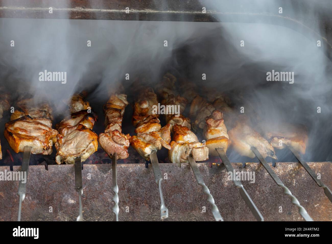 Vista ravvicinata della cucina di un delizioso barbecue in un braciere. Gustose carni di maiale e patate vengono tostate sulla griglia. Il fumo proviene dalla preparazione di un barbecue Foto Stock