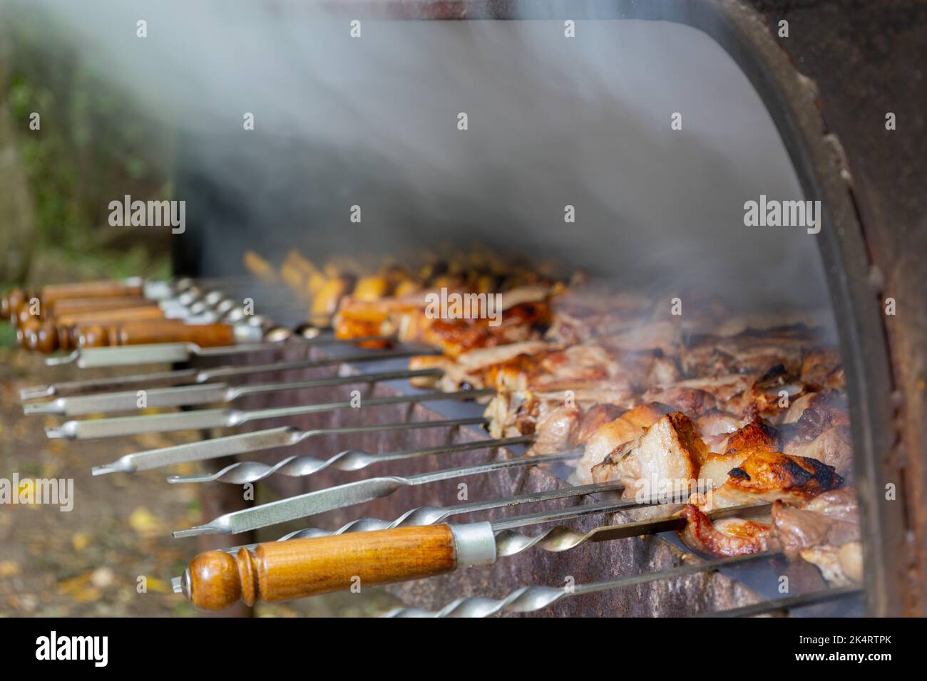 Vista ravvicinata della cucina di un delizioso barbecue in un braciere. Gustose carni di maiale e patate vengono tostate sulla griglia. Il fumo proviene dalla preparazione di un barbecue Foto Stock