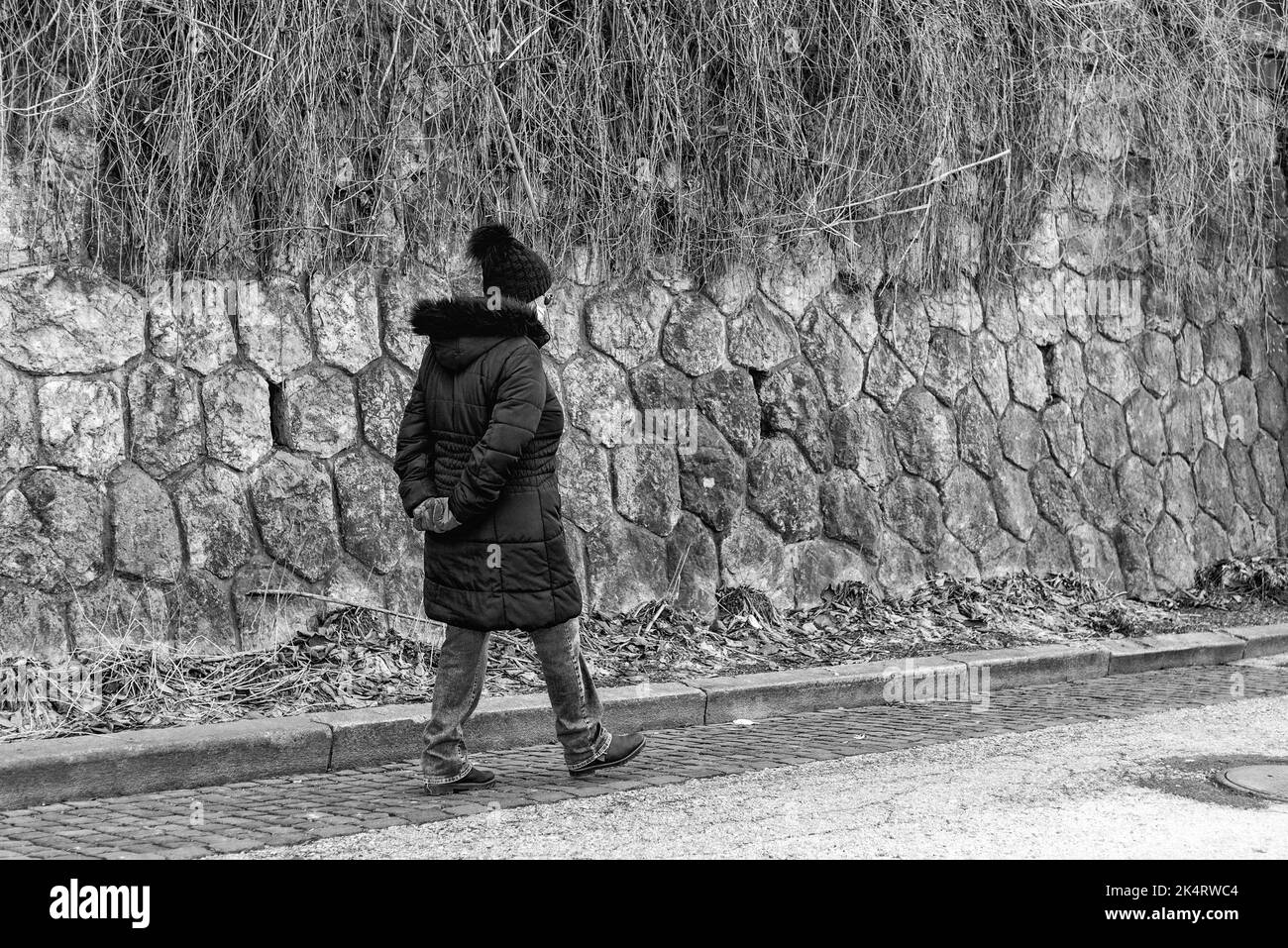 Donna anziana con maschere facciali e mani dietro la schiena camminando solitario in città Foto Stock
