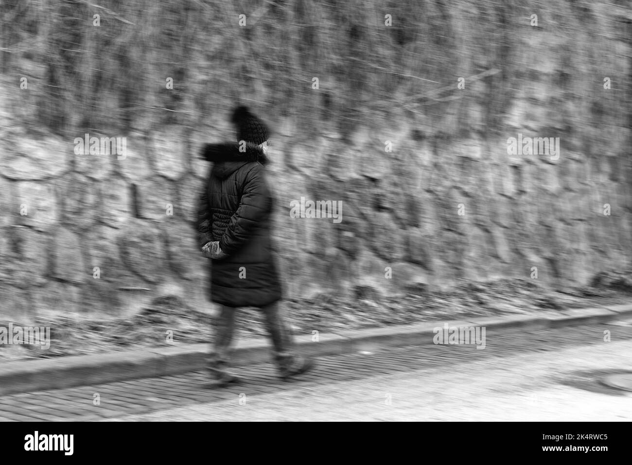 Donna anziana con maschere facciali e mani dietro la schiena camminando solitario in città Foto Stock