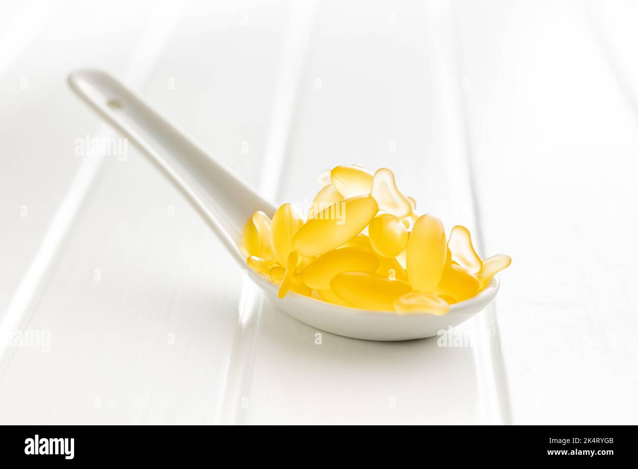 Capsule di olio di pesce. Omega 3 pillole gialle in cucchiaio sul tavolo bianco. Foto Stock