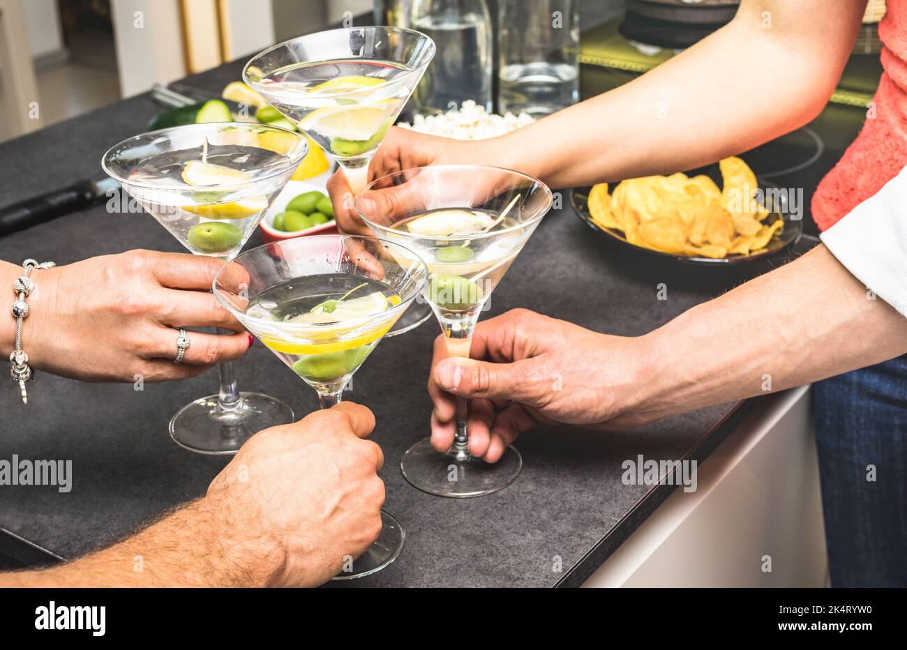 Mani di amici che si divertono a casa con aperitivo prima di cena cocktail martini e patatine olive snack - giovani che trascorrono il tempo insieme a. Foto Stock