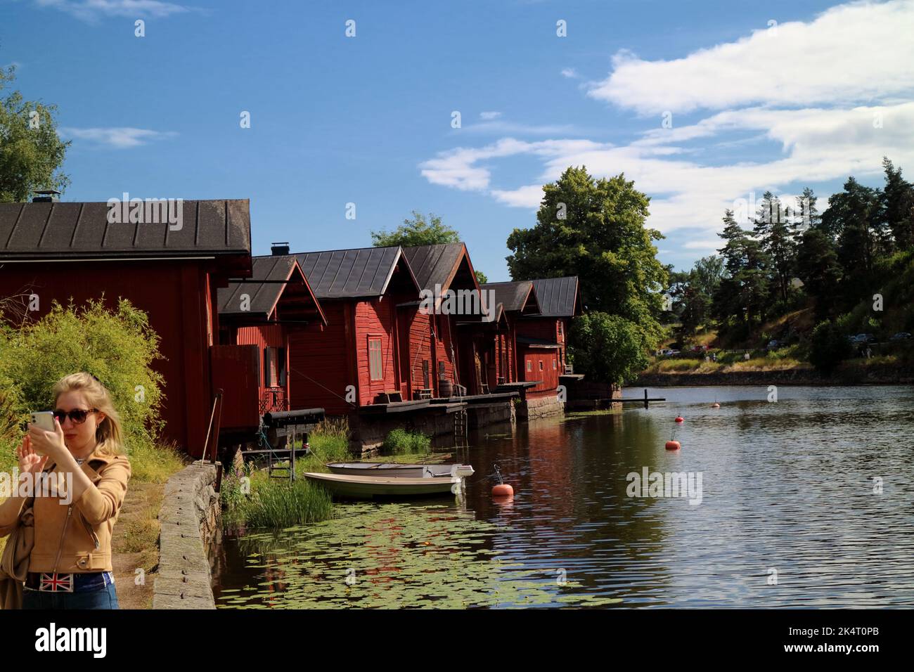Giovane donna che prende un selfie vicino al fiume in Porvoo Finlandia con vecchi capannoni di legno sullo sfondo Foto Stock
