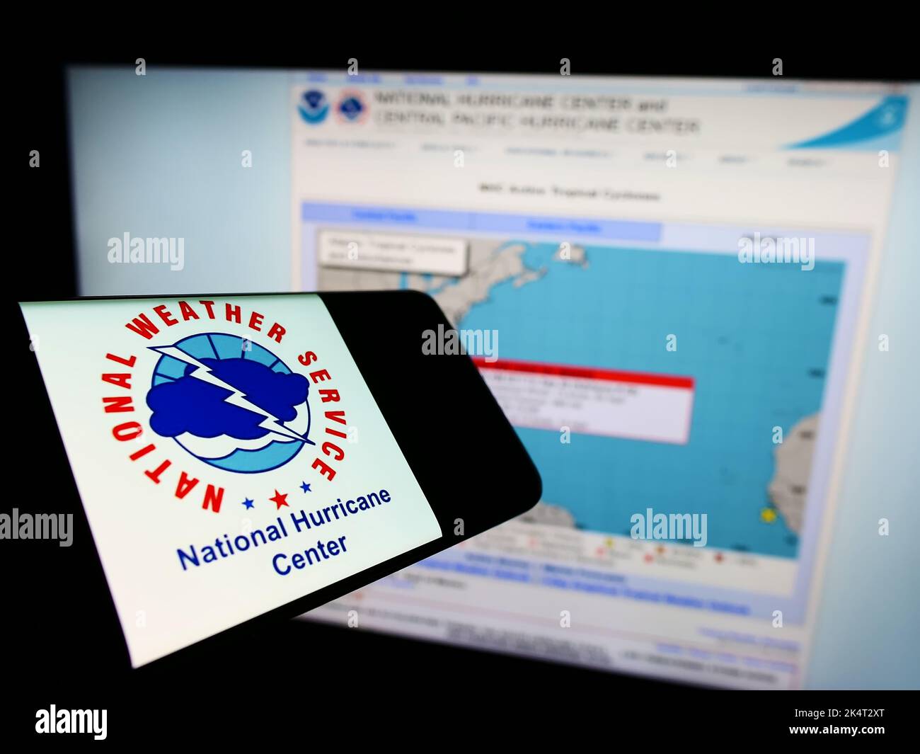 Cellulare con il logo della divisione NWS US National Hurricane Center (NHC) sullo schermo di fronte al sito web. Messa a fuoco al centro a destra del display del telefono. Foto Stock