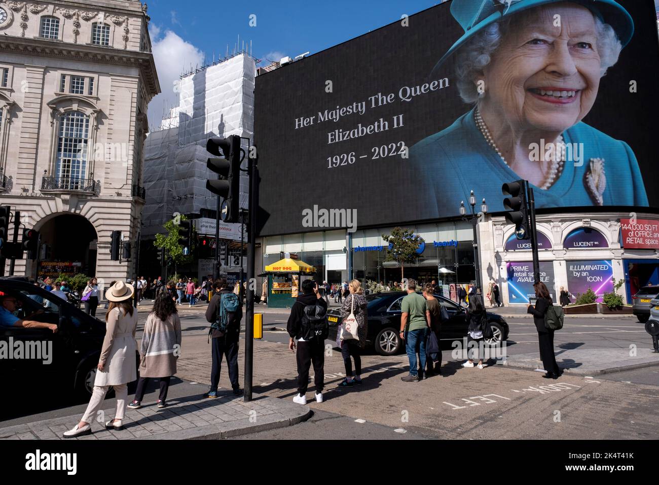 Con la pubblicità sospesa, i visitatori e i turisti a Piccadilly Circus interagiscono sotto un'immagine a colori della Regina Elisabetta II che è in mostra sugli schermi pubblicitari su larga scala il giorno successivo alla sua morte, il 9th settembre 2022 a Londra, Regno Unito. La regina, che aveva 96 anni, regnò come monarca del Regno Unito e del Commonwealth per 70 anni. Foto Stock