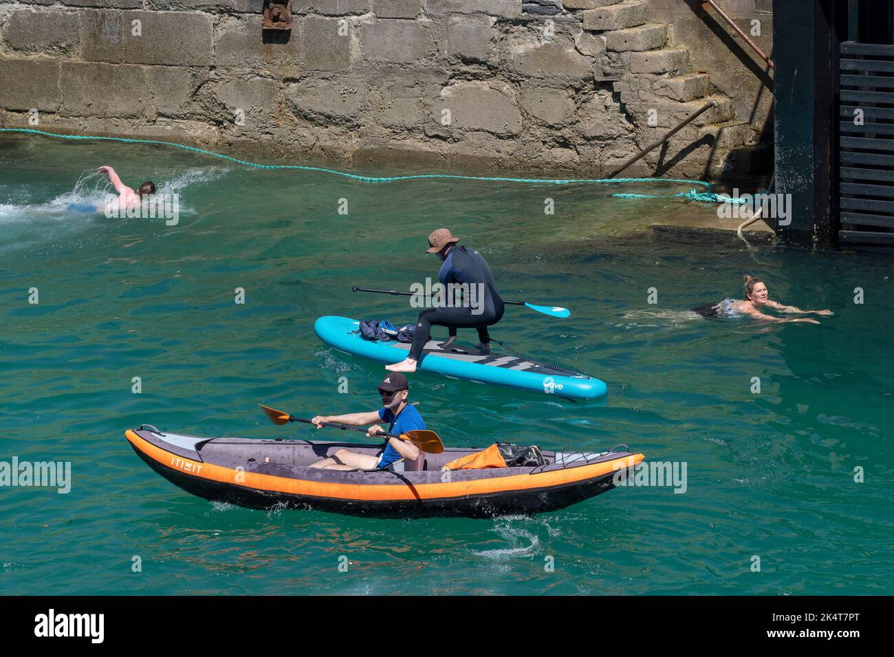 Vacanzieri che nuotano e usano un Wave Stand Up Paddleboard e un gonfiabile Itiwit canoa kayak gonfiabile nel porto di Newquay in Cornovaglia in Inghilterra Foto Stock