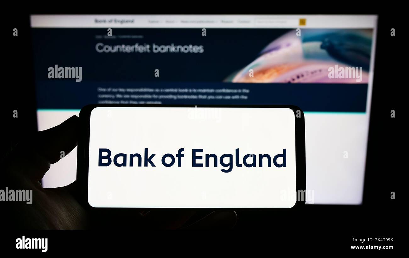 Persona che tiene il cellulare con il logo della Banca britannica emittente di Inghilterra sullo schermo di fronte alla pagina web. Messa a fuoco sul display del telefono. Foto Stock