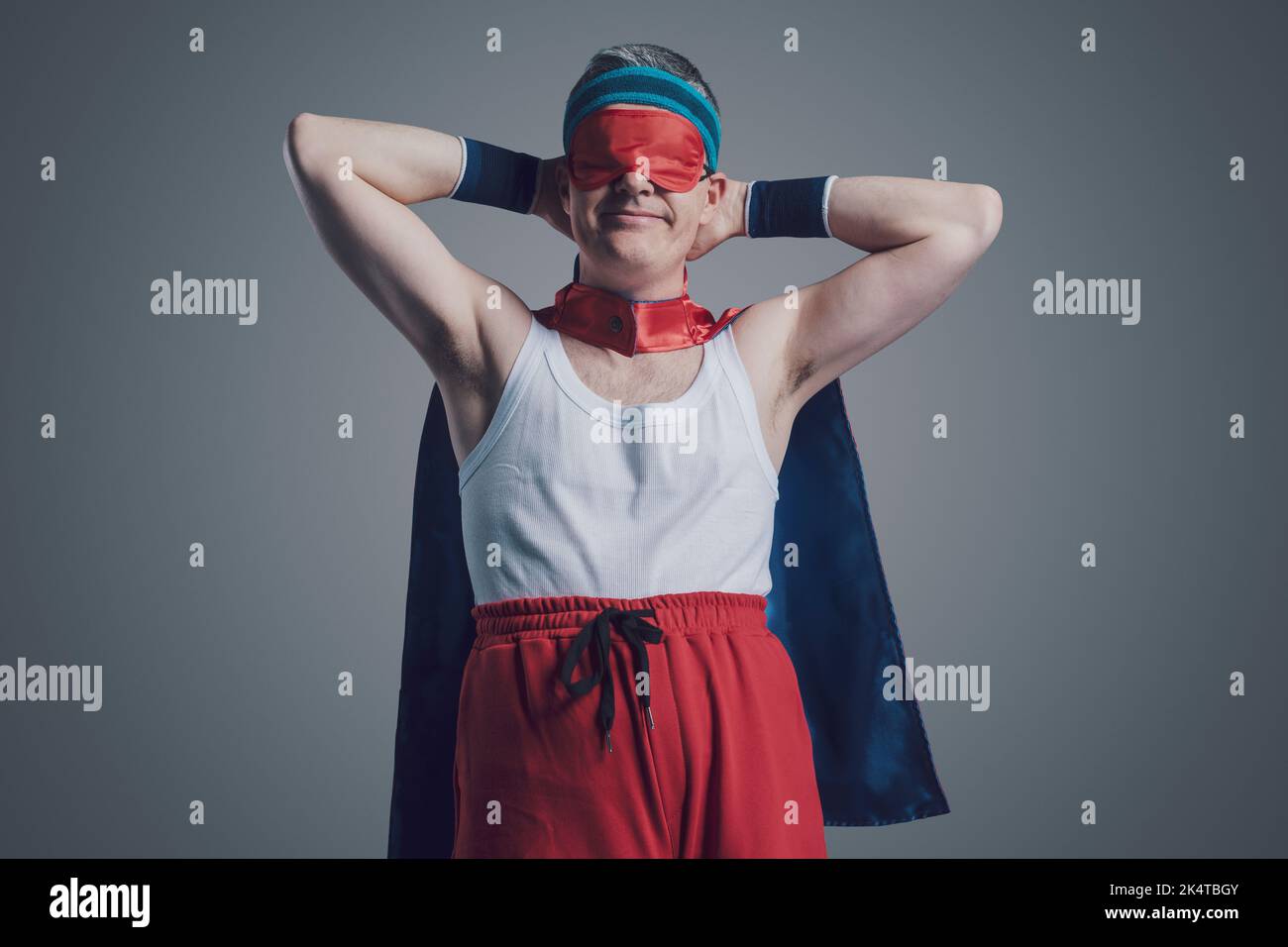 Divertente supereroe indossando una maschera di sonno sopra gli occhi e riposando con le mani dietro la testa Foto Stock