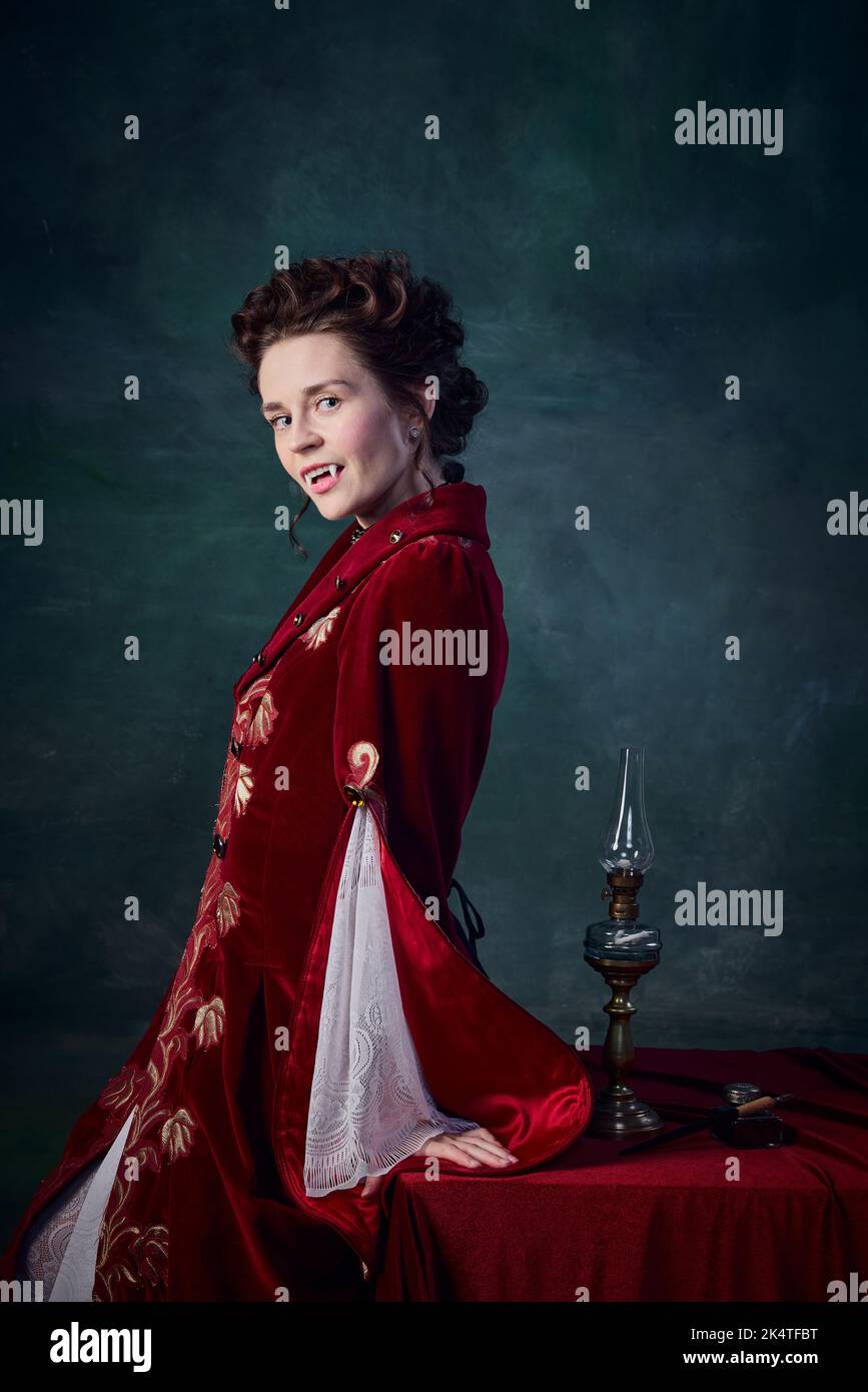 Ritratto di bella donna con pelle bianca pallida a immagine di vampiro medievale in posa elegante vestito rosso su sfondo verde scuro Foto Stock