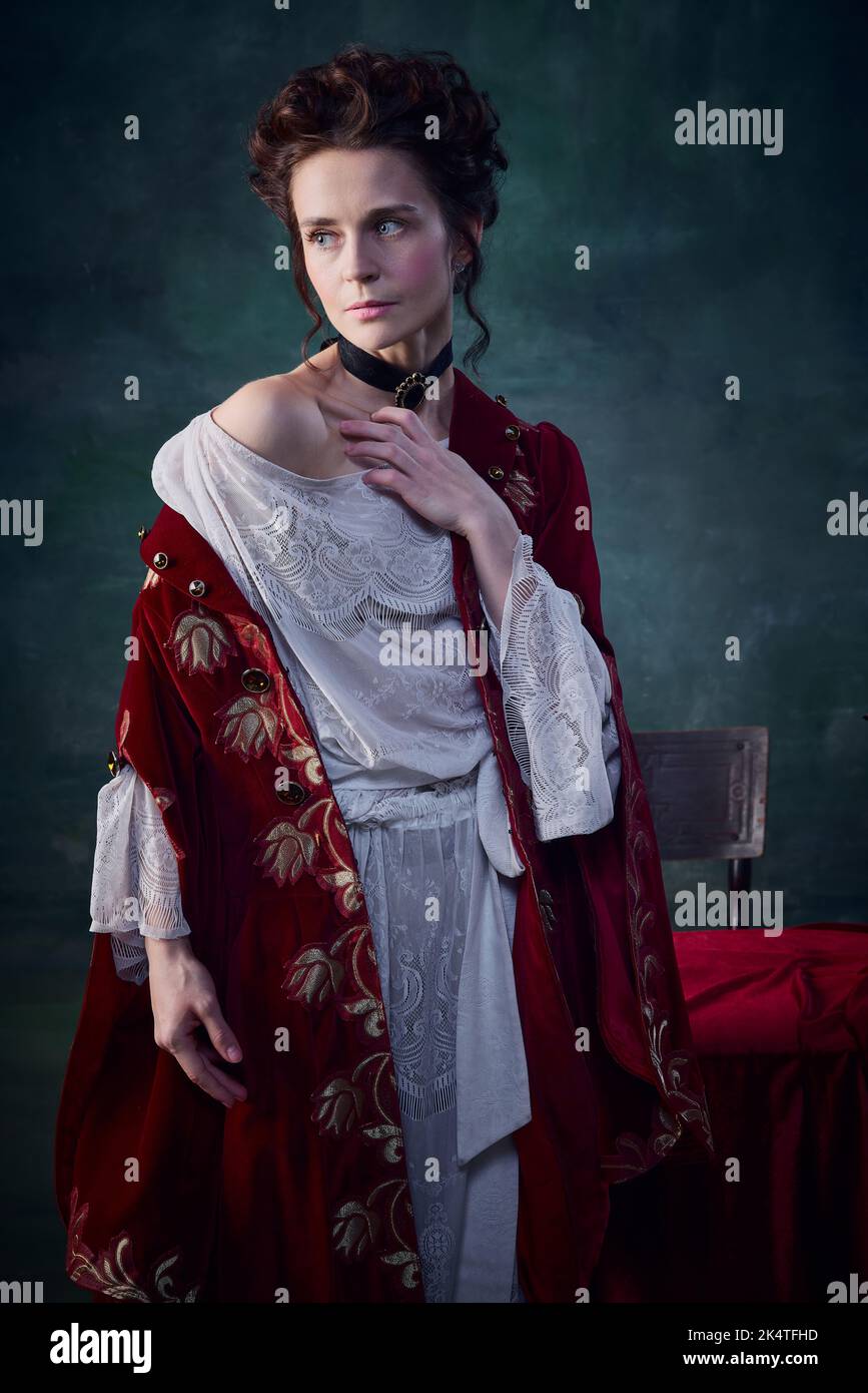 Ritratto di attraente giovane donna con pelle pallida e guance arrossanti in abito rosso velluto su sfondo verde scuro Foto Stock