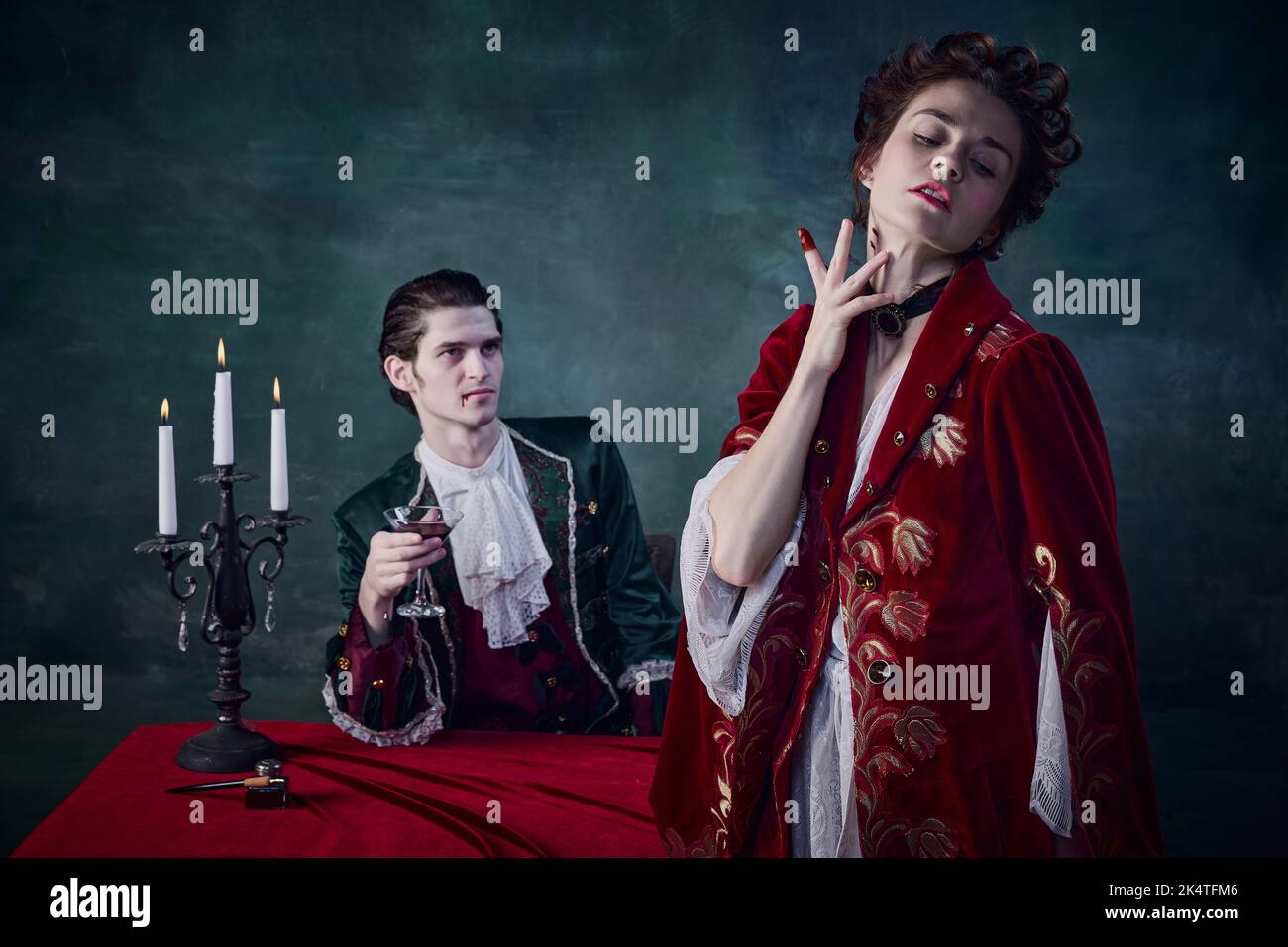 Ritratto di spaventosa famiglia di nobili vampiri, uomo e donna in costumi medievali che bevono sangue su sfondo verde scuro Foto Stock
