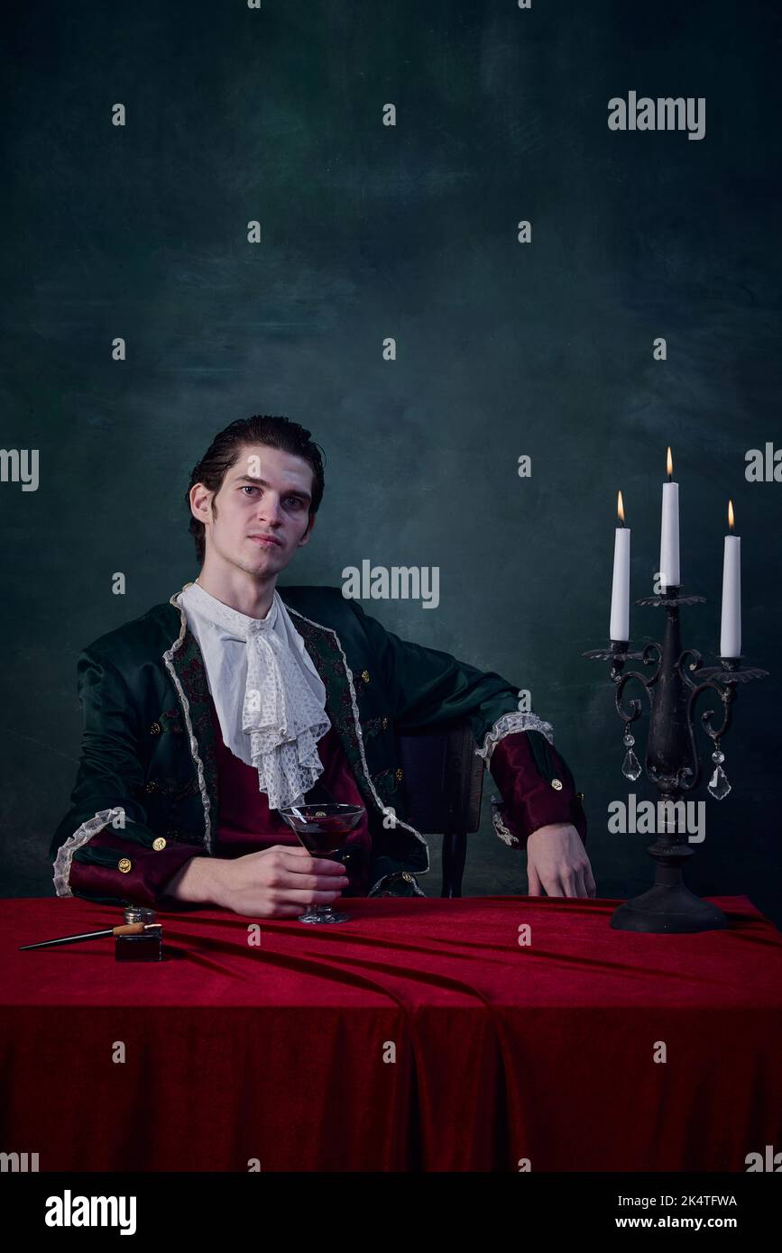 Ritratto di nobile in costume medievale d'epoca che regge un bicchiere di liquido rosso su sfondo verde scuro. Vita vampiro Foto Stock