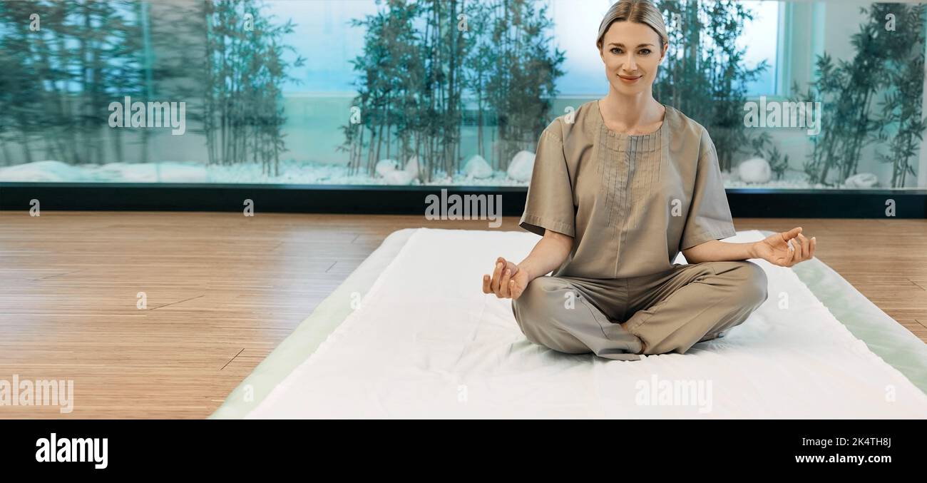 Yoga, meditazione, esercizi di respirazione. Bella donna seduta in loto posa su tappetino yoga e relax in accogliente sala meditazione Foto Stock