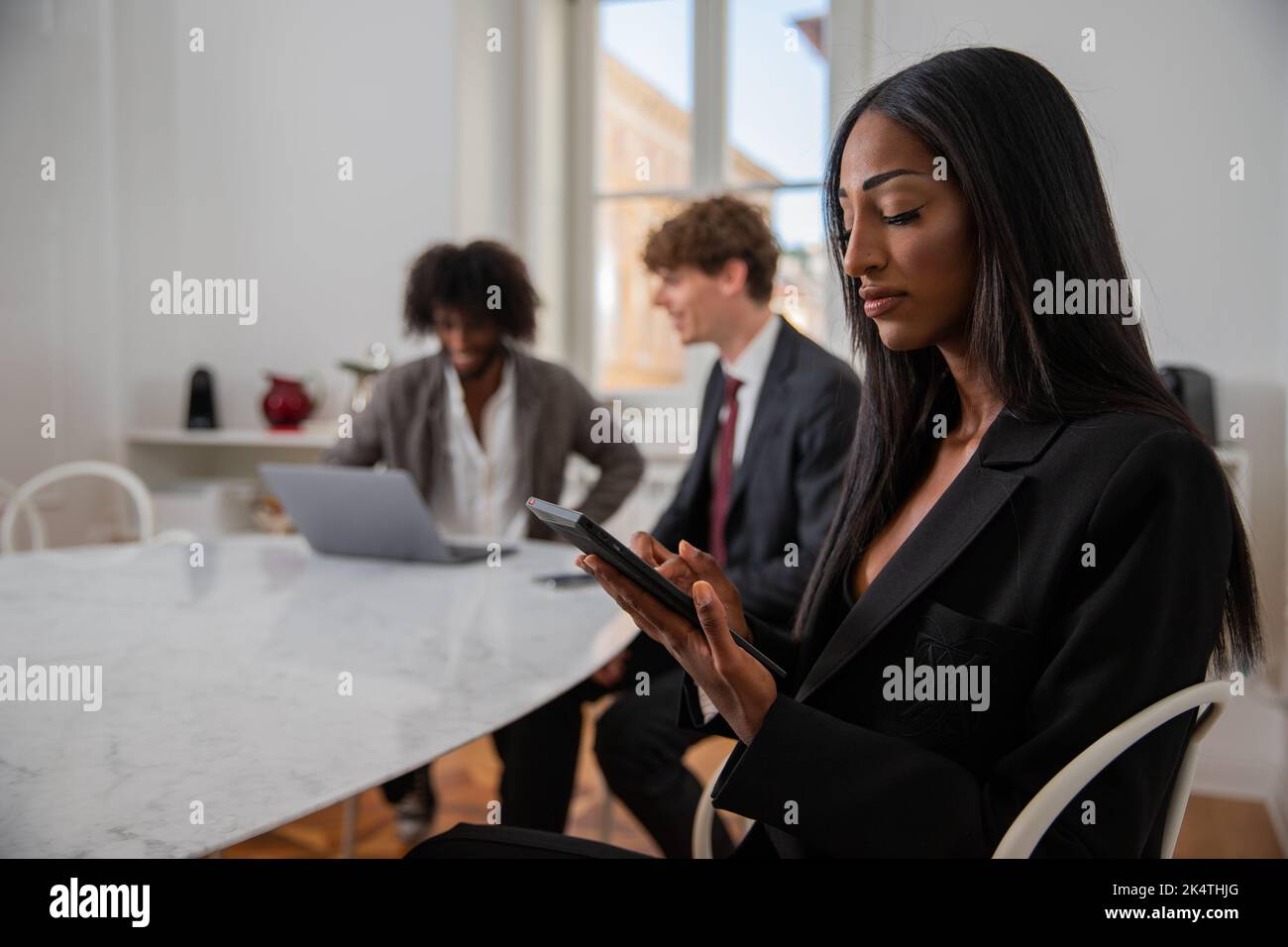 La donna d'affari africana in ufficio usa il suo tablet mentre i suoi colleghi in background lavorano, ufficio concetto Foto Stock