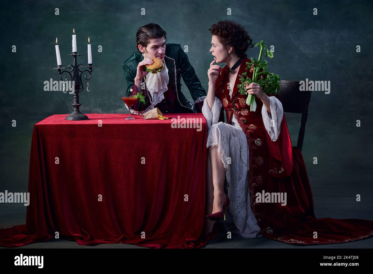 Ritratto di persone a immagine di vampiri su sfondo verde scuro. Uomo con hamburger, donna con sedano. Salute e cibo spazzatura Foto Stock