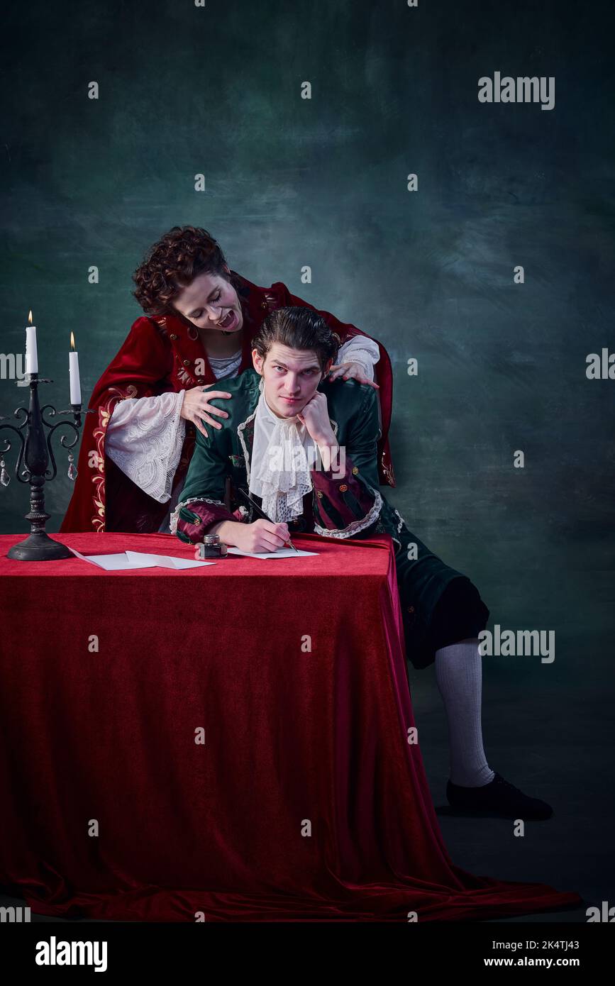 Ritratto di donna a immagine di vampiro che vuole mordere il collo dell'uomo su sfondo verde scuro. Uomo scrivere lettera Foto Stock