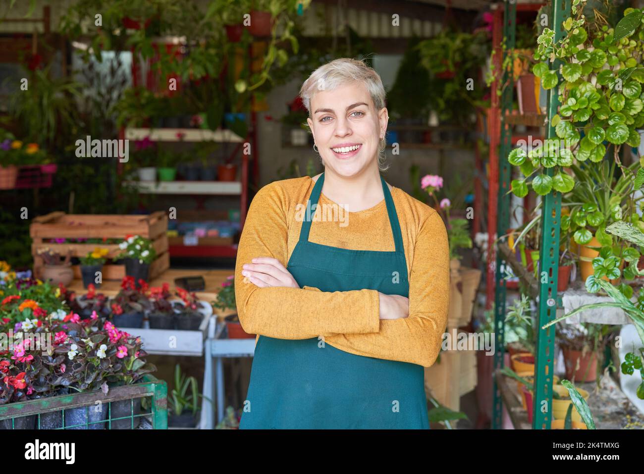 Giovane donna con braccia incrociate come fiorista fiducioso e capo nel negozio di fiori Foto Stock