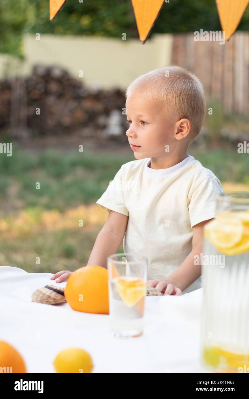 Il bambino guarda via, sulla strada. Il bambino è una bionda dagli occhi blu, in una T-shirt gialla. Sul bac sono presenti arance e sfumature gialle luminose Foto Stock