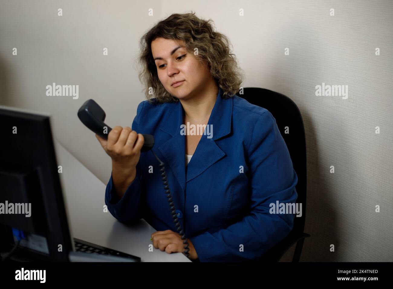 Una giovane donna siede alla scrivania in un ufficio in perplessità, non può passare attraverso il telefono. Telemarketing, agente di telemarketing, dipendente dell'ufficio. Foto Stock